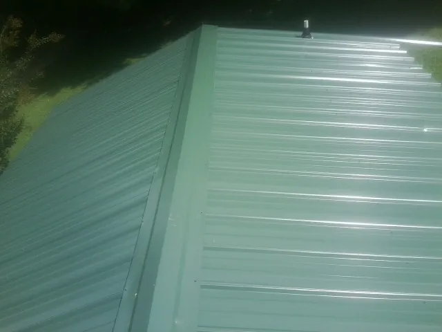 New green metal panels meeting at the ridge of a roof — Flat Roof Repair work by our crew in Bath