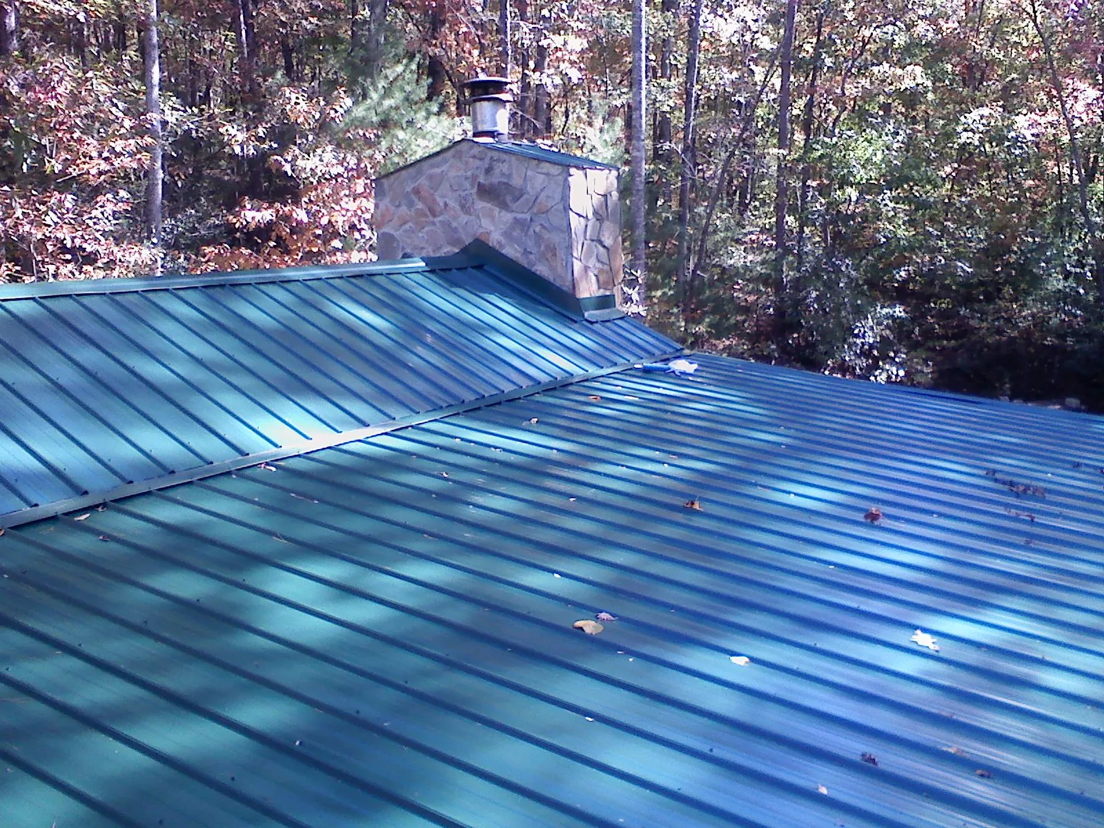 New green metal roof and stone chimney surrounded by autumn woods in Bath